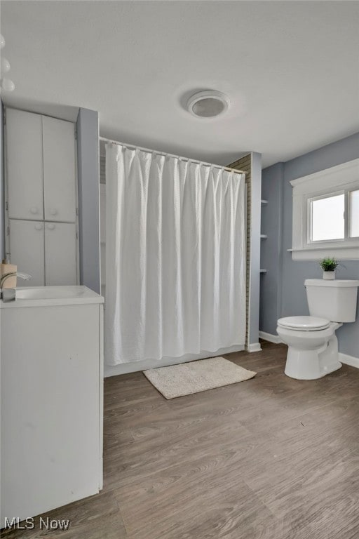 full bath with a shower with shower curtain, toilet, wood finished floors, and baseboards