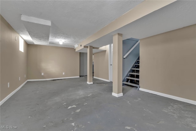 finished below grade area with stairway, a textured ceiling, and baseboards