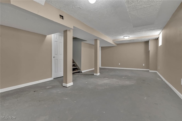 finished basement with stairway, baseboards, and a textured ceiling