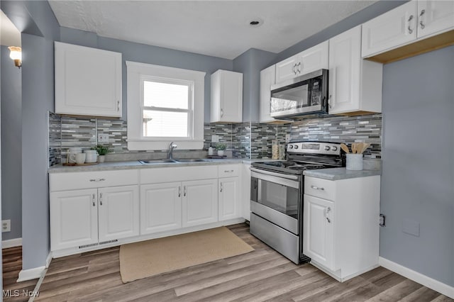 kitchen with baseboards, visible vents, a sink, light wood-style floors, and appliances with stainless steel finishes