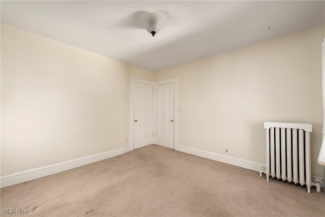 carpeted empty room with radiator and baseboards