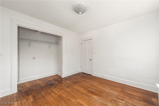 unfurnished bedroom featuring hardwood / wood-style floors, baseboards, and a closet