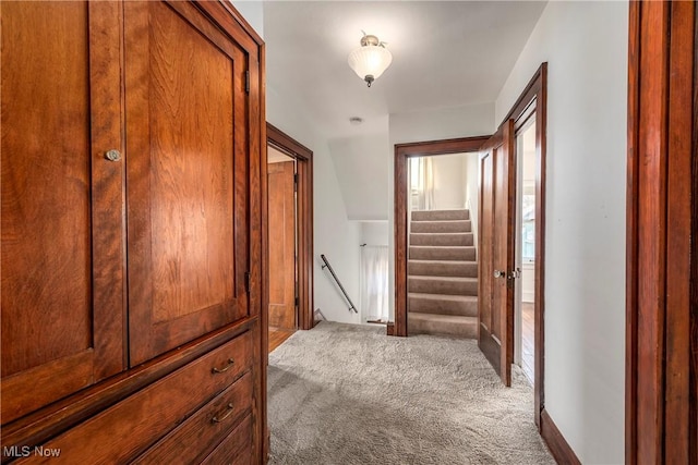 corridor with an upstairs landing, stairway, and carpet floors