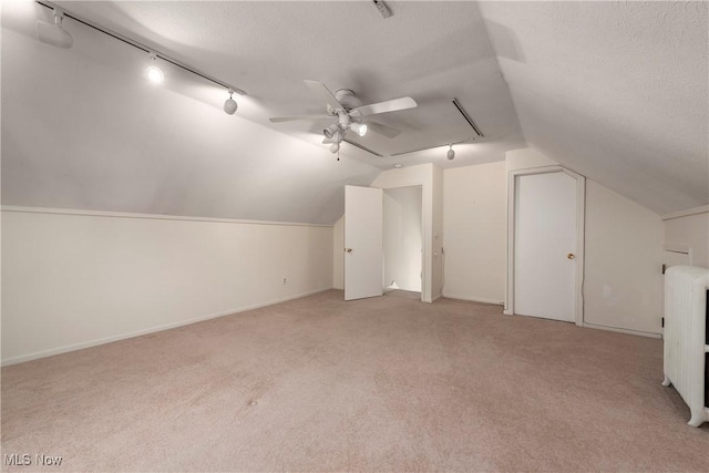 additional living space with radiator, light colored carpet, vaulted ceiling, a textured ceiling, and a ceiling fan