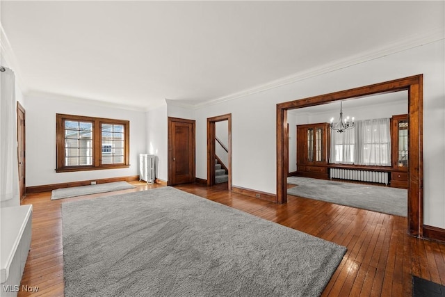 unfurnished living room featuring an inviting chandelier, ornamental molding, radiator heating unit, and hardwood / wood-style flooring