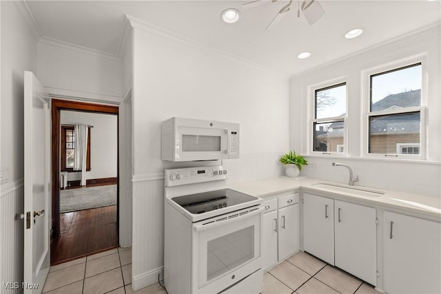 kitchen featuring white appliances, light tile patterned floors, a ceiling fan, a wainscoted wall, and a sink