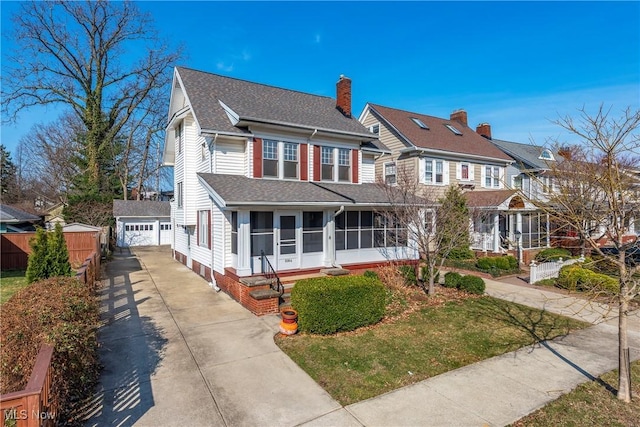 view of front of home featuring a shingled roof, fence, concrete driveway, a sunroom, and an outbuilding