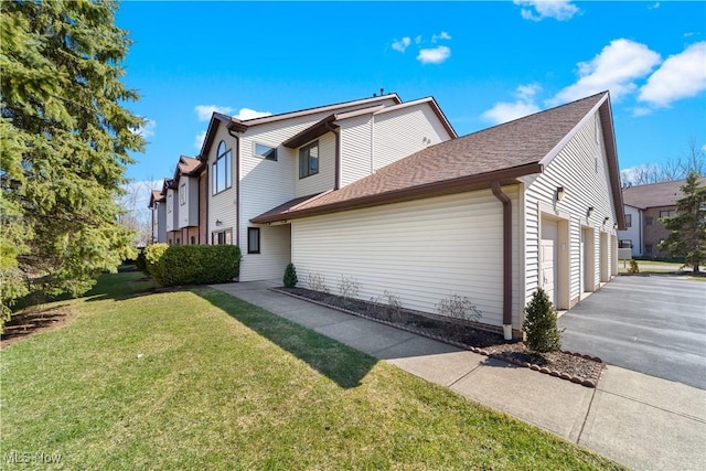 view of side of property featuring aphalt driveway, a lawn, an attached garage, and a shingled roof