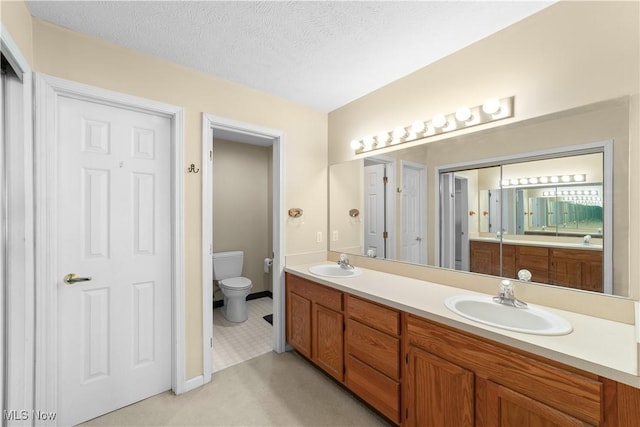 full bathroom with a sink, toilet, double vanity, and a textured ceiling