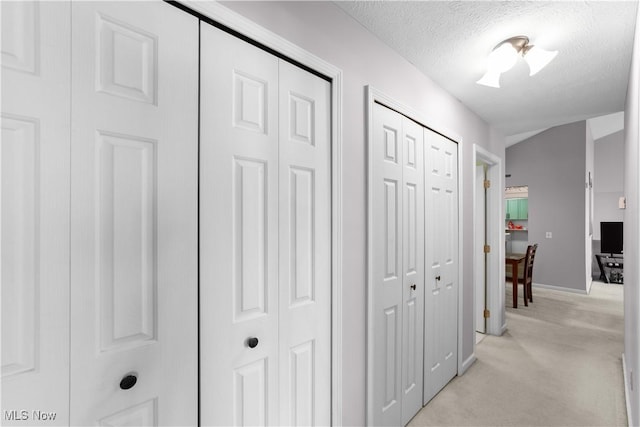 hallway featuring light colored carpet, vaulted ceiling, and a textured ceiling