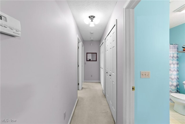 hall featuring a wall unit AC, light colored carpet, baseboards, and a textured ceiling