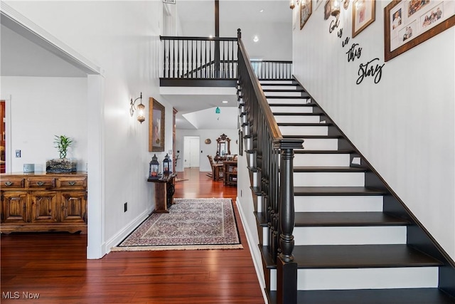 stairway with baseboards, wood finished floors, and a towering ceiling