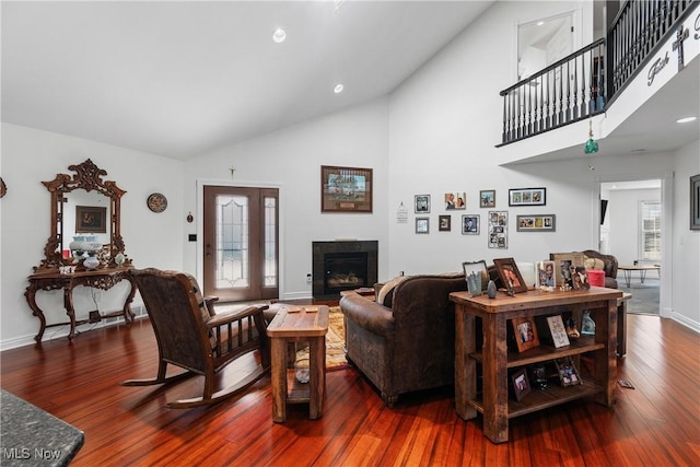 living room featuring baseboards, wood-type flooring, high vaulted ceiling, and a glass covered fireplace