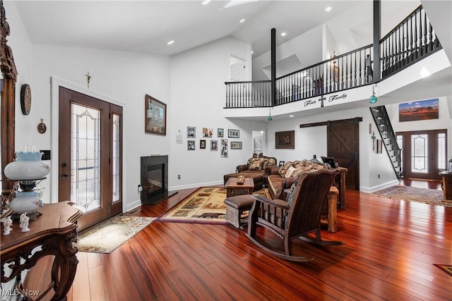 living room with high vaulted ceiling, hardwood / wood-style flooring, a glass covered fireplace, a barn door, and french doors