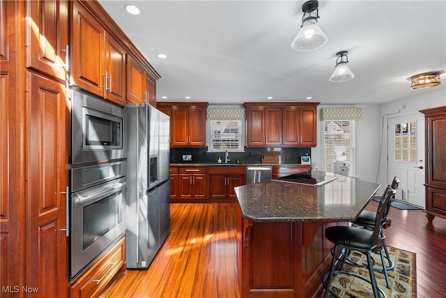 kitchen with a breakfast bar area, a sink, wood-type flooring, appliances with stainless steel finishes, and tasteful backsplash