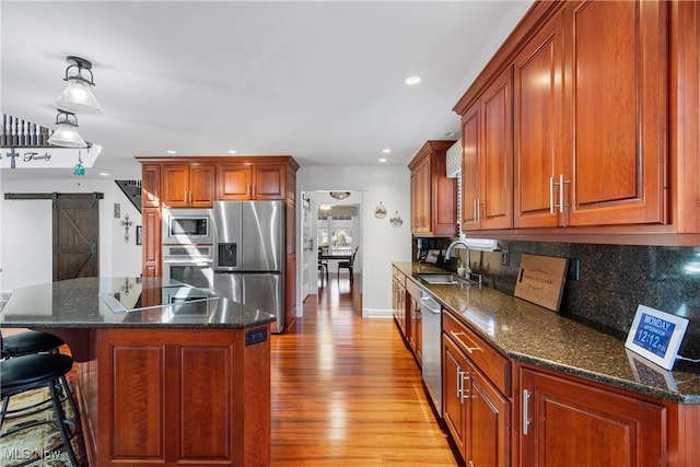 kitchen with light wood-style flooring, a sink, tasteful backsplash, a barn door, and appliances with stainless steel finishes