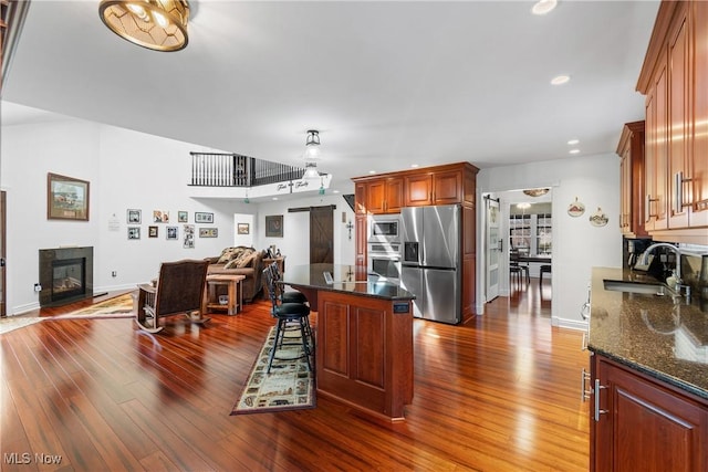 kitchen featuring dark wood-style floors, a sink, appliances with stainless steel finishes, a kitchen breakfast bar, and open floor plan