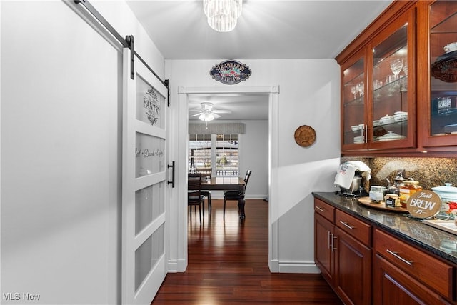 corridor featuring a barn door, baseboards, dark wood-type flooring, and a chandelier