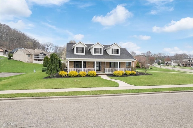 new england style home with brick siding, a front yard, a residential view, and covered porch