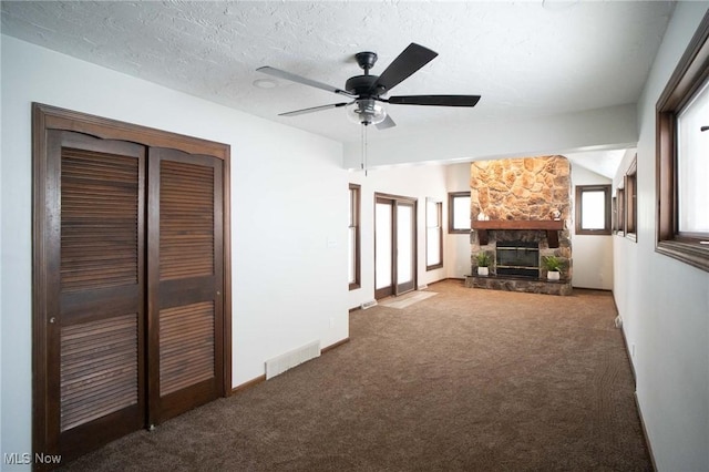 unfurnished living room featuring a stone fireplace, lofted ceiling, visible vents, and carpet floors