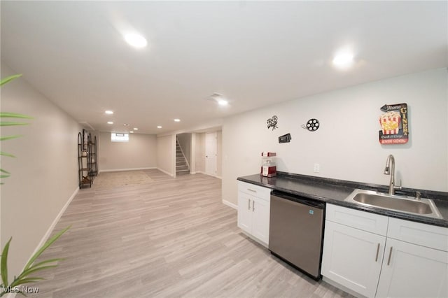 kitchen with dark countertops, light wood-style flooring, stainless steel dishwasher, white cabinetry, and a sink