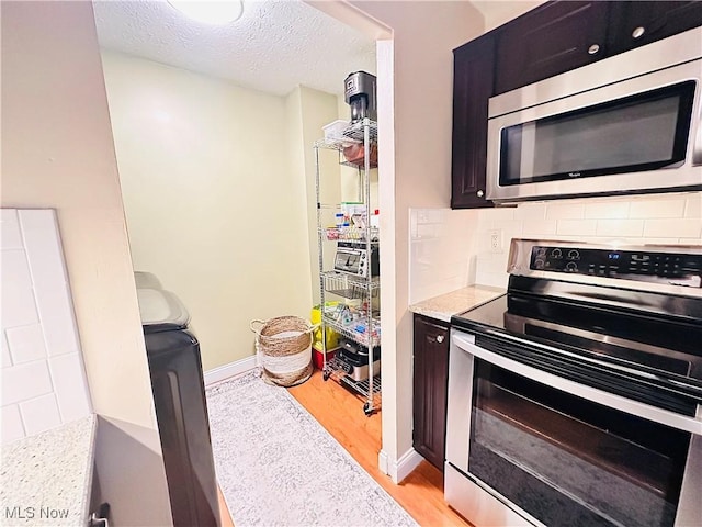 kitchen with light wood-style flooring, a textured ceiling, appliances with stainless steel finishes, light countertops, and decorative backsplash