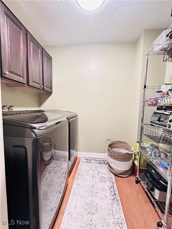 laundry room with cabinet space, washer and dryer, a textured ceiling, and light wood-type flooring