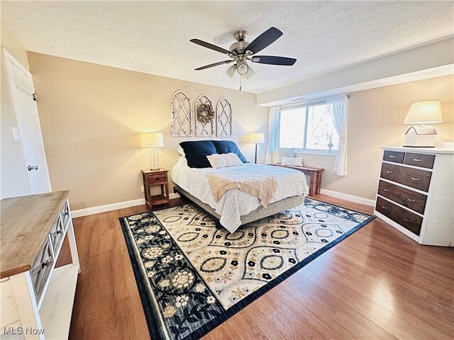 bedroom with light wood-style flooring, a textured ceiling, baseboards, and ceiling fan