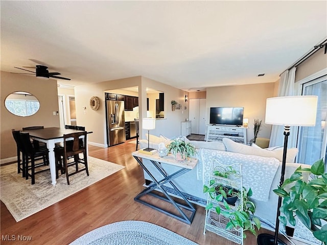 living area featuring visible vents, baseboards, light wood-style floors, and a ceiling fan