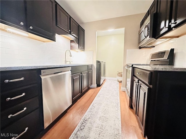 kitchen featuring washing machine and clothes dryer, a sink, appliances with stainless steel finishes, and dark cabinets