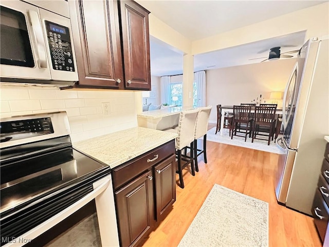 kitchen featuring light wood-type flooring, a ceiling fan, backsplash, dark brown cabinetry, and appliances with stainless steel finishes