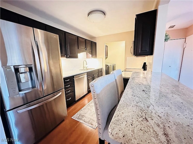 kitchen featuring light wood-type flooring, a sink, tasteful backsplash, stainless steel appliances, and washing machine and clothes dryer