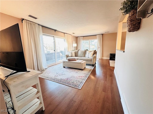 living room featuring visible vents, a textured ceiling, baseboards, and wood finished floors