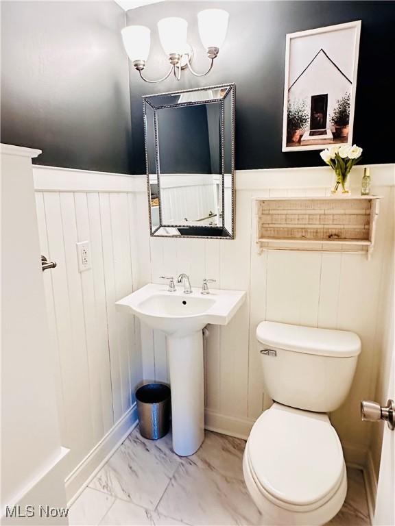 bathroom featuring a sink, a wainscoted wall, toilet, and marble finish floor