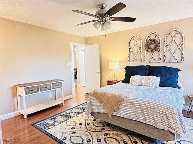 bedroom featuring baseboards, a textured ceiling, wood finished floors, and a ceiling fan