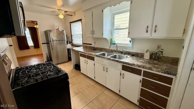 kitchen with dark countertops, gas range oven, freestanding refrigerator, light tile patterned flooring, and a sink