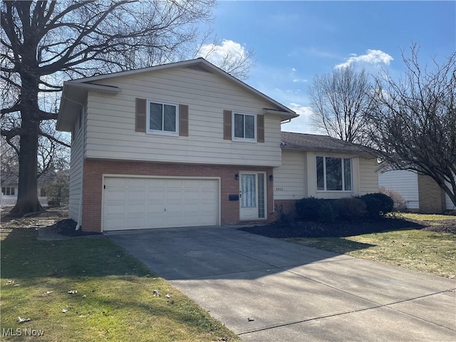 split level home featuring concrete driveway, a garage, brick siding, and a front yard