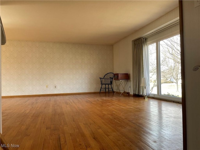 unfurnished room featuring wallpapered walls, hardwood / wood-style flooring, and baseboards