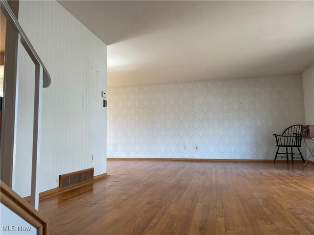 spare room with visible vents, wallpapered walls, baseboards, and wood finished floors