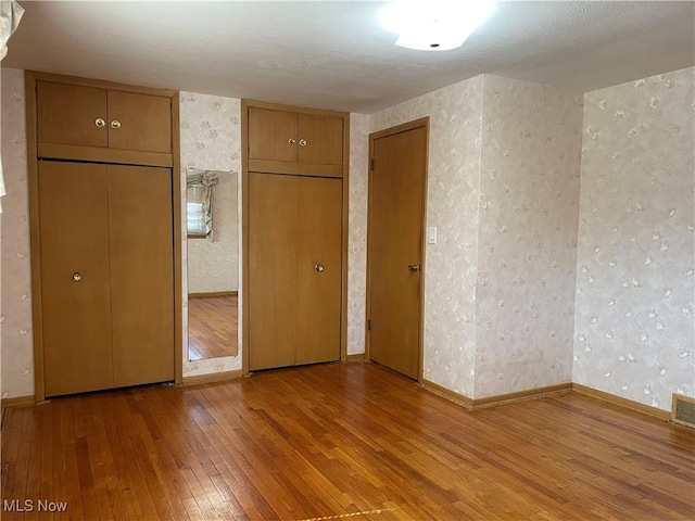 unfurnished bedroom with wallpapered walls, hardwood / wood-style flooring, visible vents, and baseboards