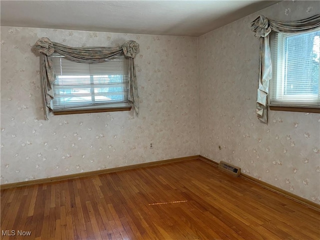 empty room featuring a wealth of natural light, visible vents, baseboards, and wood-type flooring