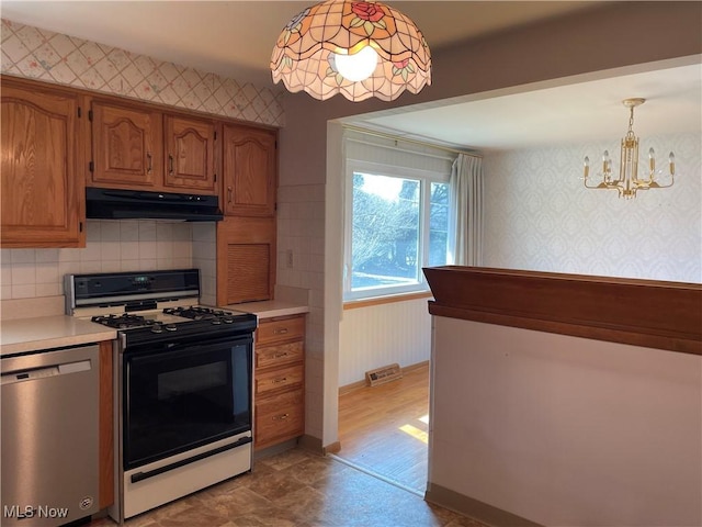 kitchen with wallpapered walls, light countertops, gas range oven, under cabinet range hood, and stainless steel dishwasher