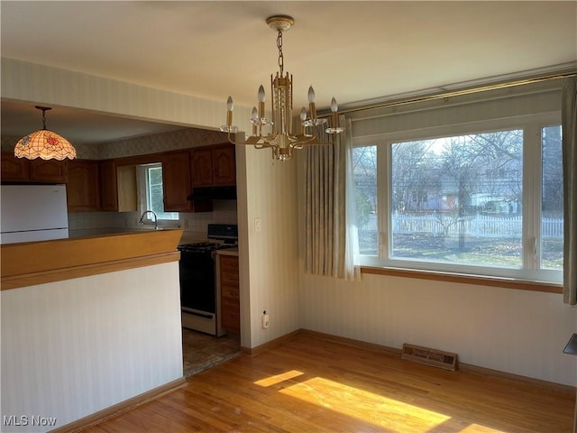 kitchen featuring visible vents, light wood-type flooring, a sink, freestanding refrigerator, and gas stove