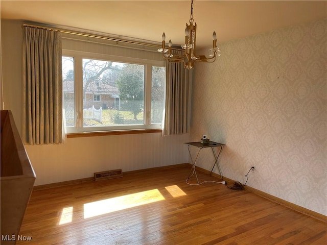 spare room with a chandelier, visible vents, wallpapered walls, and wood finished floors