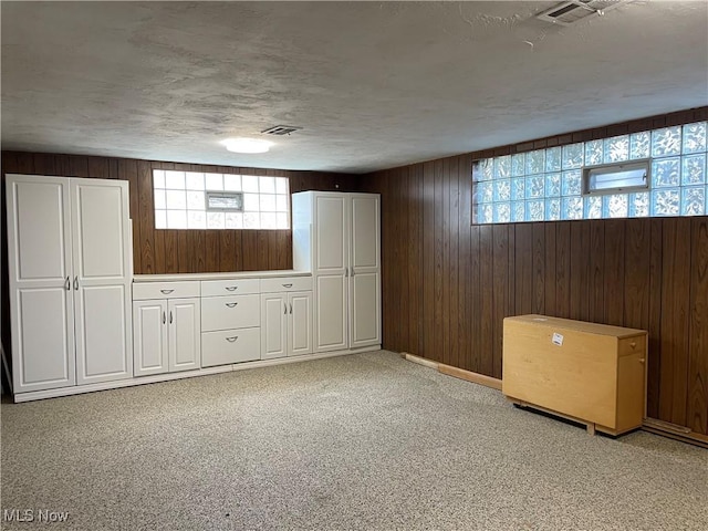 basement featuring visible vents, wood walls, a textured ceiling, and light colored carpet