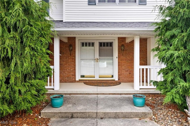 view of exterior entry with brick siding, a porch, and a shingled roof