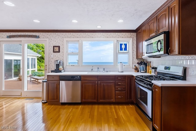 kitchen featuring wallpapered walls, light countertops, appliances with stainless steel finishes, light wood-style floors, and a sink