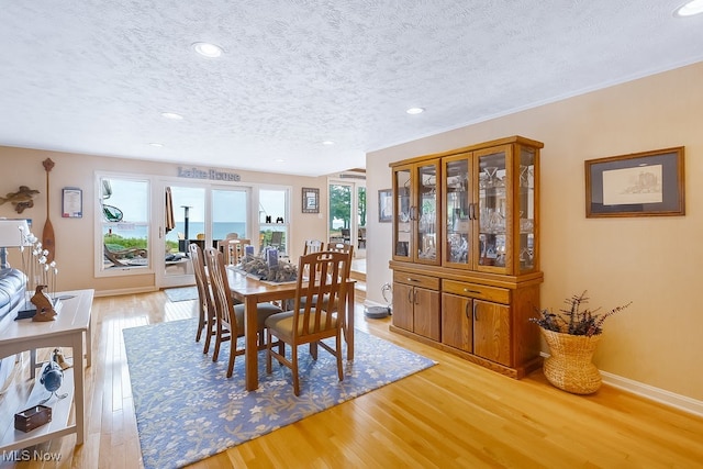 dining area featuring light wood finished floors, a healthy amount of sunlight, a textured ceiling, and baseboards