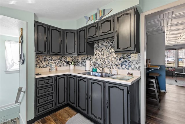 kitchen with dark wood-type flooring, baseboards, light countertops, decorative backsplash, and a sink