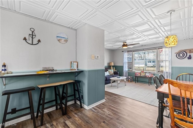 dining area with a wainscoted wall, an ornate ceiling, a ceiling fan, and wood finished floors